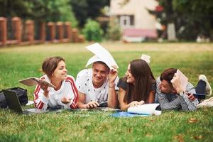 annoiato e avendo divertimento. gruppo di giovane studenti nel casuale Abiti su verde erba a giorno foto