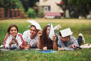 annoiato e avendo divertimento. gruppo di giovane studenti nel casuale Abiti su verde erba a giorno foto