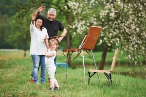 saluta a fotografare. nonna e nonno si divertono all'aperto con la nipote. concezione della pittura foto