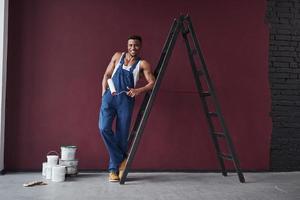 uomo divertente e felice. il giovane lavoratore afroamericano in uniforme blu ha un lavoro da fare foto