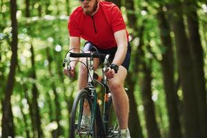guarda sulla mano. il ciclista in bicicletta è sulla strada asfaltata nella foresta in una giornata di sole foto