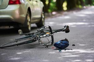 il luogo della pausa. bicicletta e incidente d'auto color argento sulla strada nella foresta durante il giorno foto