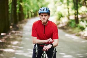 ritratto di uomo barbuto. il ciclista in bicicletta è sulla strada asfaltata nella foresta in una giornata di sole foto