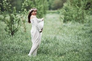 futuro genitore. bella donna incinta in abito fare una passeggiata all'aperto. bruna positiva foto