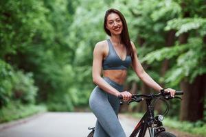 una sola persona. ciclista femminile in piedi con la bici su strada asfaltata nella foresta durante il giorno foto