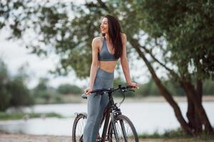 finalmente ho raggiunto la mia destinazione. ciclista femminile con una buona forma del corpo in piedi con la sua bici sulla spiaggia durante il giorno foto