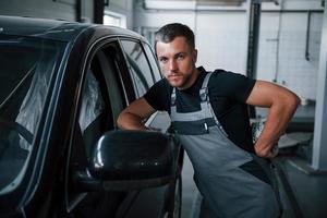 giovane meccanico sta in casa vicino nero macchina. dopo riparazione automobile foto