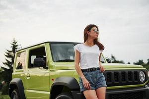 sta vicino nuovo veicolo. bella donna nel il verde moderno auto in posa per il telecamera foto