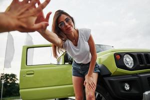 giovane ragazza nel estate Abiti contento per vedere voi. verde auto dietro a foto