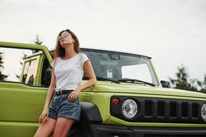 sta vicino nuovo veicolo. bella donna nel il verde moderno auto in posa per il telecamera foto