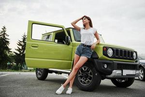 sta vicino nuovo veicolo. bella donna nel il verde moderno auto in posa per il telecamera foto