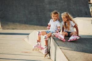 caldo tempo atmosferico. su il rampa per estremo gli sport. Due poco ragazze con rullo pattini all'aperto avere divertimento foto