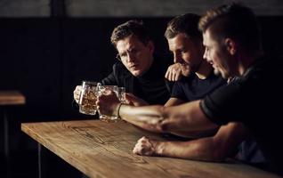 tre gli sport fan nel un' bar Guardando calcio. con birra nel mani foto