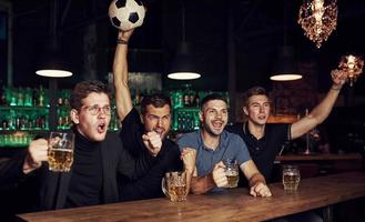 con calcio sfera. è un' obiettivo. festeggiare vittoria. tre gli sport fan nel un' bar Guardando calcio con birra nel mani foto