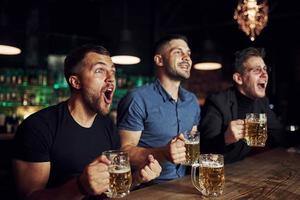 festeggiare vittoria. tre gli sport fan nel un' bar Guardando calcio. con birra nel mani foto
