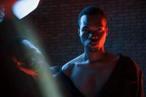 fiducioso tipo. futuristico neon illuminazione. giovane africano americano uomo nel il studio foto
