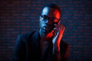 avendo conversazione di utilizzando Telefono. futuristico neon illuminazione. giovane africano americano uomo nel il studio foto