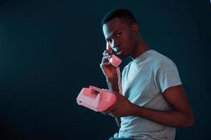 retrò rosa colorato Telefono. futuristico neon illuminazione. giovane africano americano uomo nel il studio foto