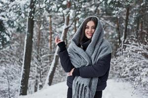freddo boschi e caldo ragazza. ritratto di affascinante donna nel il nero giacca e grigio sciarpa nel il inverno foresta foto