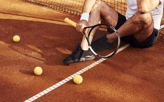 seduta e assunzione un' rompere. vicino su Visualizza di anziano uomo nel bianca camicia e nero allegro pantaloncini quello è su tennis Tribunale foto