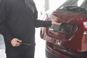 posteriore parte di veicolo. uomo nel ufficiale Abiti sta vicino il suo nuovo auto nel automobile salone foto