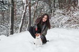 petting il cane. sorridente brunetta avendo divertimento mentre a piedi con sua cane nel il inverno parco foto