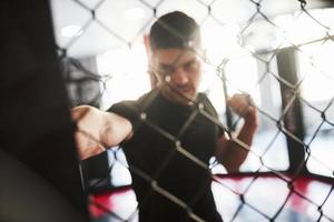 sfocato immagine. forte uomo è boxe nel il Palestra dietro a il recinzione. ha quotidiano esercizio foto