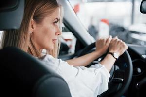 andiamo spingere il pedale per il metallo. bellissimo bionda ragazza seduta nel il nuovo auto con moderno nero interno foto