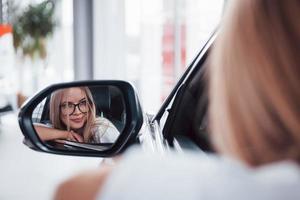 focalizzata foto. donna nel bicchieri guardare in lato specchio di un' moderno veicolo nel il salone foto