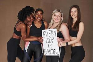 avendo simpatico volta. gruppo di Multi etnico donne in piedi nel il studio contro Marrone sfondo foto