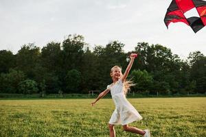 foto nel movimento. contento ragazza nel bianca Abiti avere divertimento con aquilone nel il campo. bellissimo natura