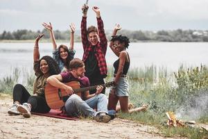 gioioso squadra di gli amici. gruppo di persone avere picnic su il spiaggia. avendo divertimento a fine settimana tempo foto