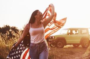 ragazza corre inoltrare. amici avere simpatico fine settimana all'aperto vicino il loro verde auto con Stati Uniti d'America bandiera foto