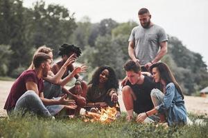 uomo parla con interesse. gruppo di persone avere picnic su il spiaggia. amici avere divertimento a fine settimana tempo foto