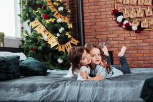 abbracciare ogni Altro. Due allegro femmina bambini dire bugie su il letto con nuovo anno decorazioni e vacanza albero foto