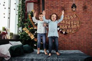 bambino festa nel il simpatico guardare Natale decorato camera. allegro bambini avendo divertimento e salto su il letto con decorativo vacanza sfondo foto