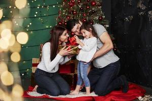 apertura il regalo. è quello è che cosa io pensare. bello famiglia si siede vicino il Natale albero con regalo scatole su inverno sera, godendo il tempo la spesa insieme foto