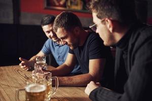 tre maschio amici nel il sbarra. supporto triste amico. unità di le persone. con birra su il tavolo foto
