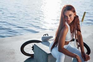 vicino alla bici. fitness donna che si riposa vicino al lago durante il giorno. bella luce del sole foto