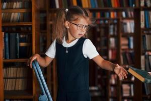 scuola ragazza su il scala nel biblioteca pieno di libri. formazione scolastica concezione foto