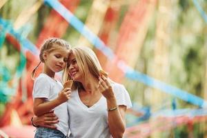 mangiare ghiaccio crema. allegro poco ragazza sua madre avere un' bene tempo nel il parco insieme vicino attrazioni foto