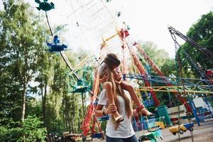 a piedi con figlia su il le spalle. allegro poco ragazza sua madre avere un' bene tempo nel il parco insieme vicino attrazioni foto