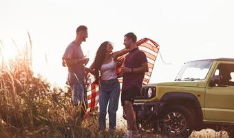 avendo conversazione. amici avere simpatico fine settimana all'aperto vicino il loro verde auto con Stati Uniti d'America bandiera foto