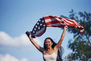 femmina patriota corre con Stati Uniti d'America bandiera nel mani all'aperto nel il campo contro blu cielo foto