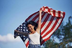 femmina patriota corre con Stati Uniti d'America bandiera nel mani all'aperto nel il campo contro blu cielo foto