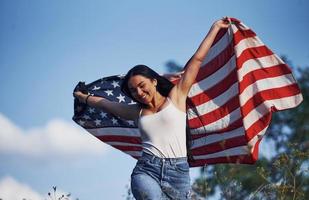 femmina patriota corre con Stati Uniti d'America bandiera nel mani all'aperto nel il campo contro blu cielo foto