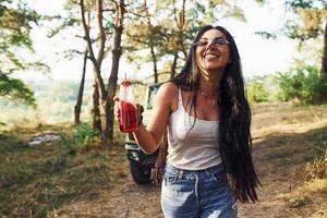 bionda con alcool nel mano avere un' camminare nel il foresta contro verde camionetta foto