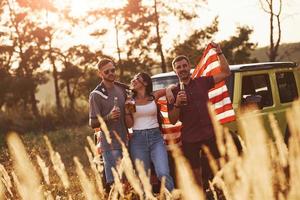 con alcool nel mani. amici avere simpatico fine settimana all'aperto vicino il loro verde auto con Stati Uniti d'America bandiera foto