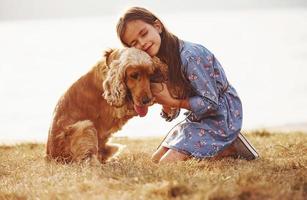 Tenere di il mani. carino poco ragazza avere un' camminare con sua cane all'aperto a soleggiato giorno foto