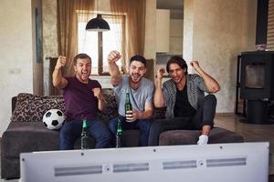 eccitato tre amici Guardando calcio su tv a casa insieme foto